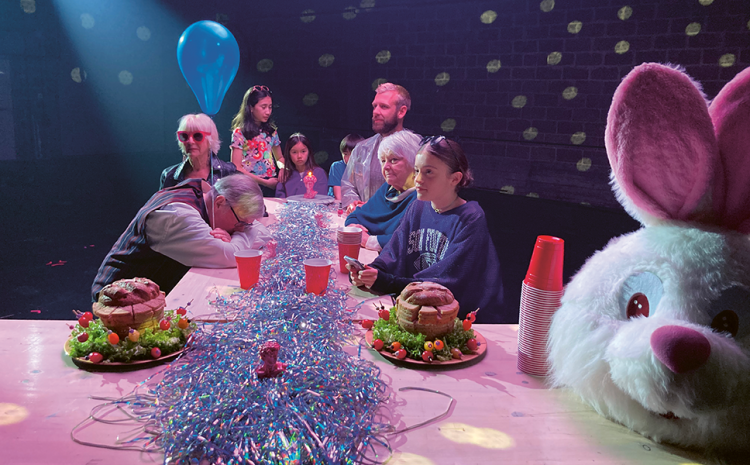Photo d'une table de fête autour de laquelle sont assis des femmes, hommes et enfants