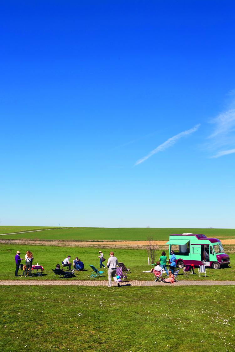 prairie verte sur fond de ciel bleu, musiciens au second plan avec une roulotte